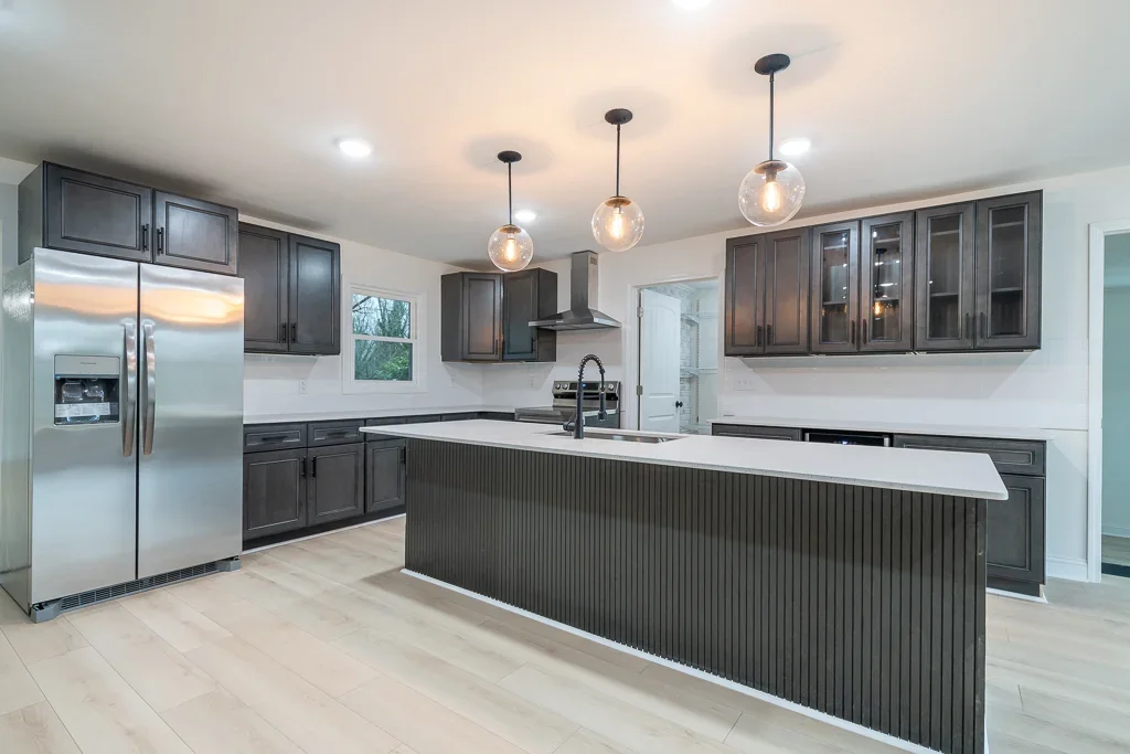 Dark cabinetry kitchen with white quartz island, glass pendants, stainless appliances