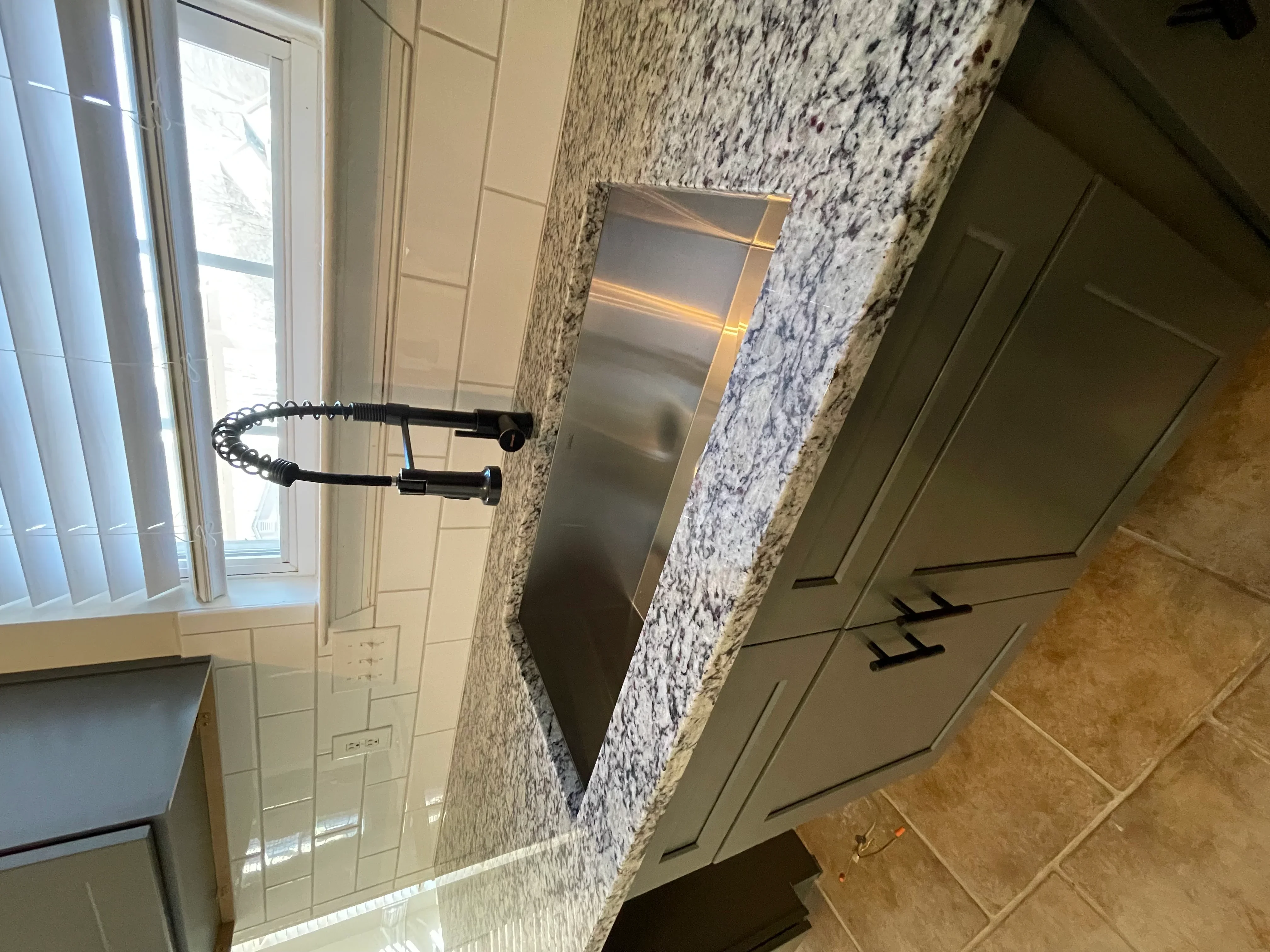 Granite countertop with stainless steel sink and black gooseneck faucet in updated kitchen