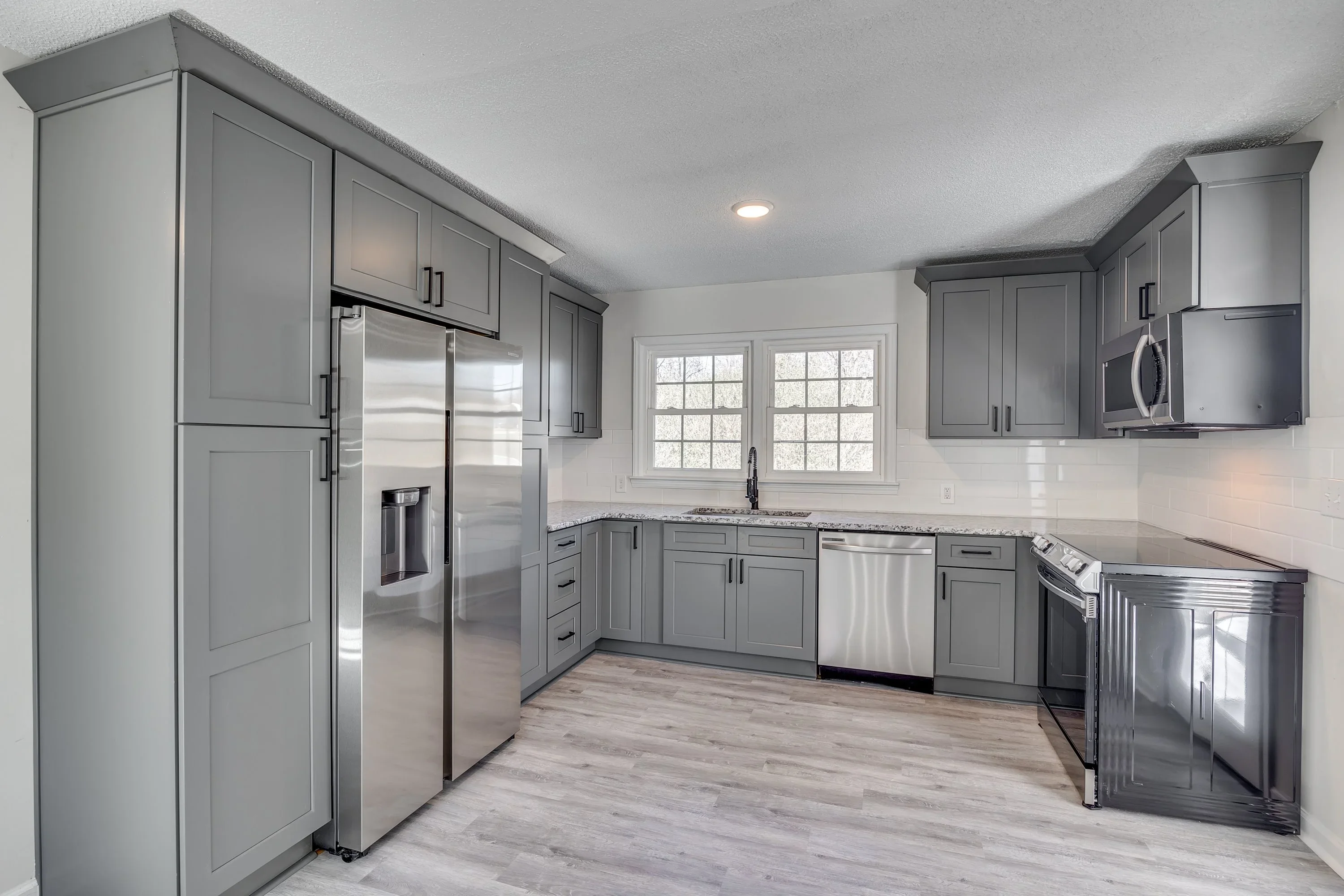 Gray shaker cabinets, granite counters, stainless steel appliances, subway tile backsplash, wood flooring