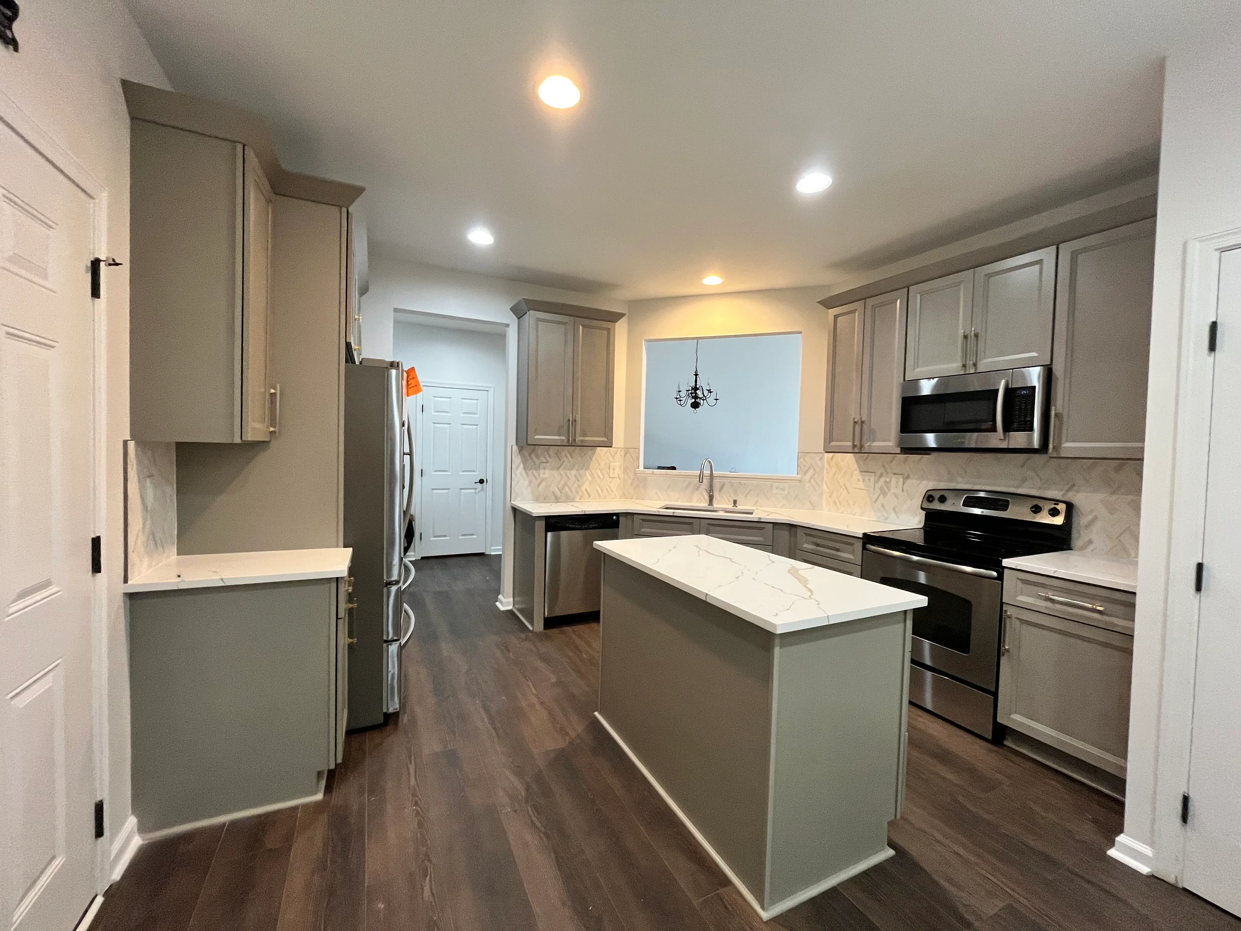 Gray cabinetry kitchen with white quartz island, stainless steel appliances, and herringbone backsplash