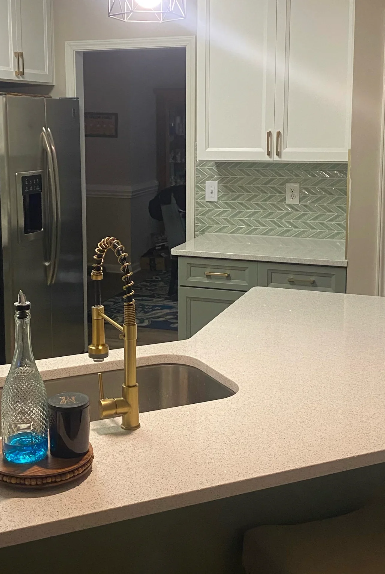 Modern kitchen with quartz countertops, herringbone tile backsplash, white cabinets, and brass faucet
