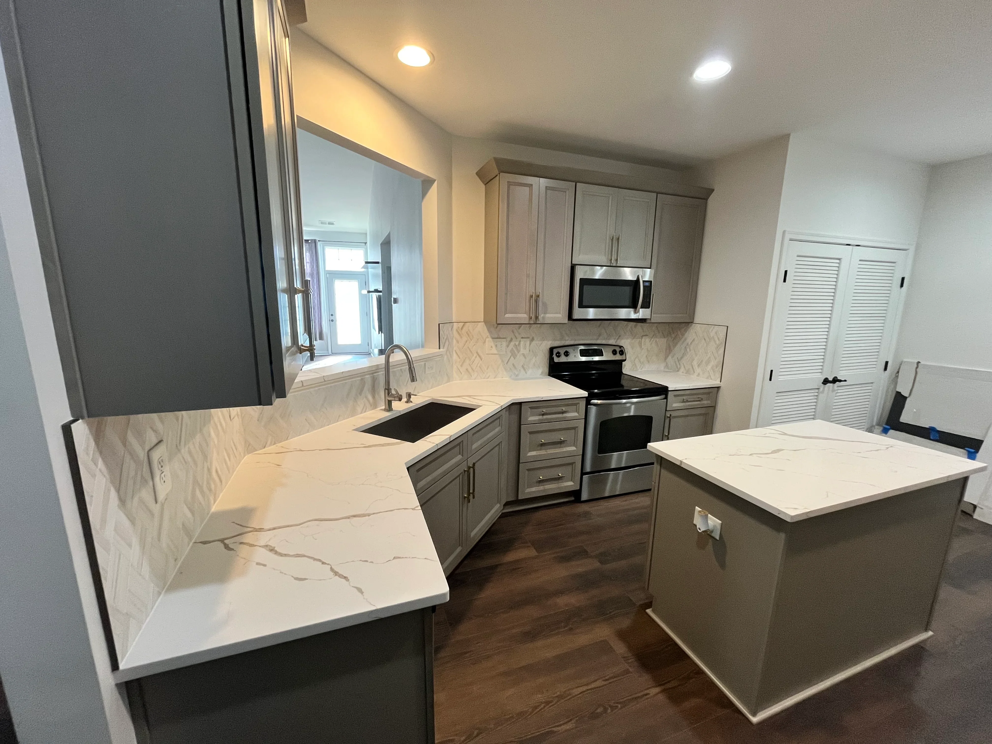 Modern kitchen with gray cabinets, marble quartz counters, stainless steel appliances, and island