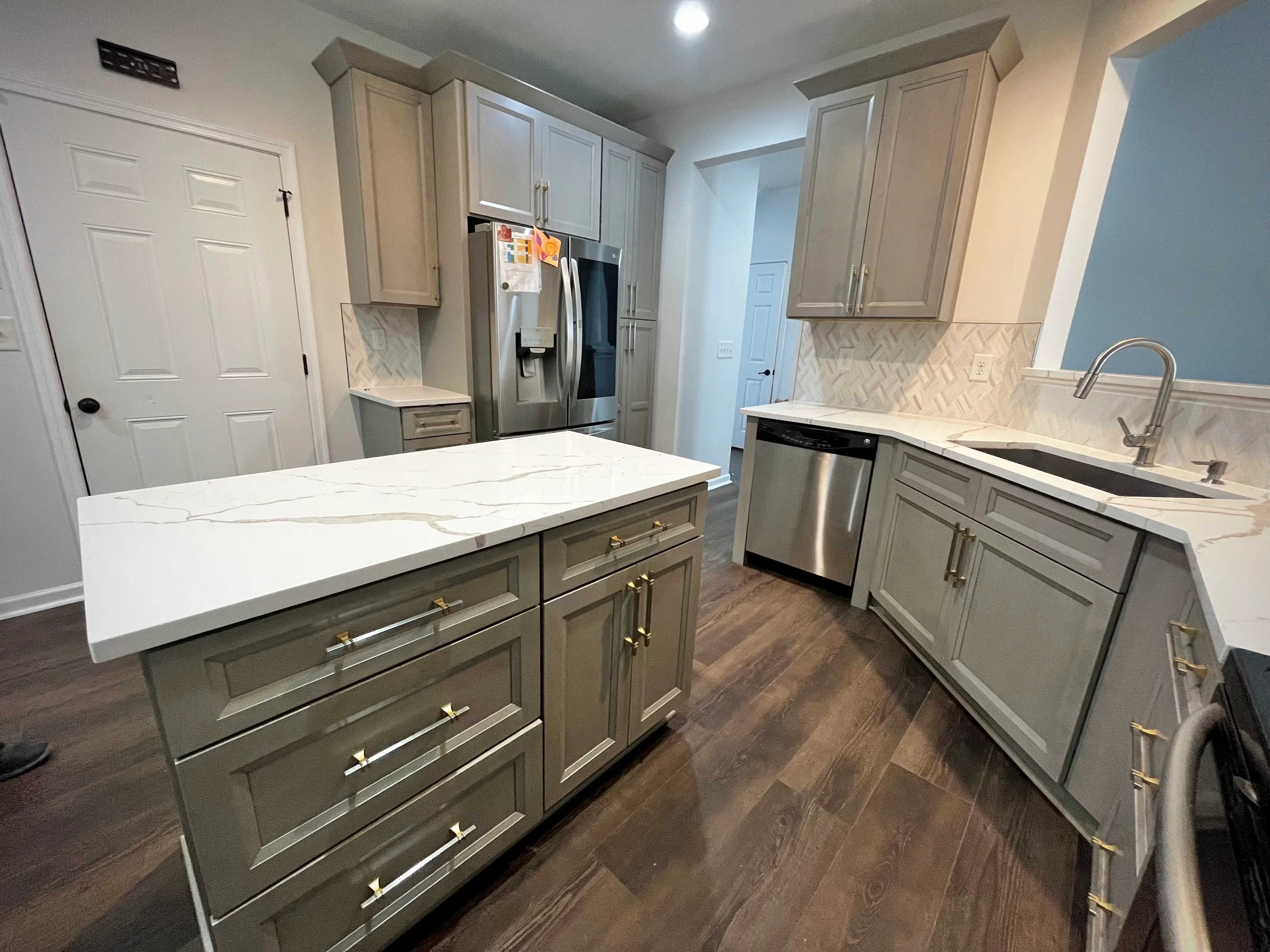 Modern kitchen with greige cabinets, white quartz counters, island, stainless appliances, and herringbone backsplash