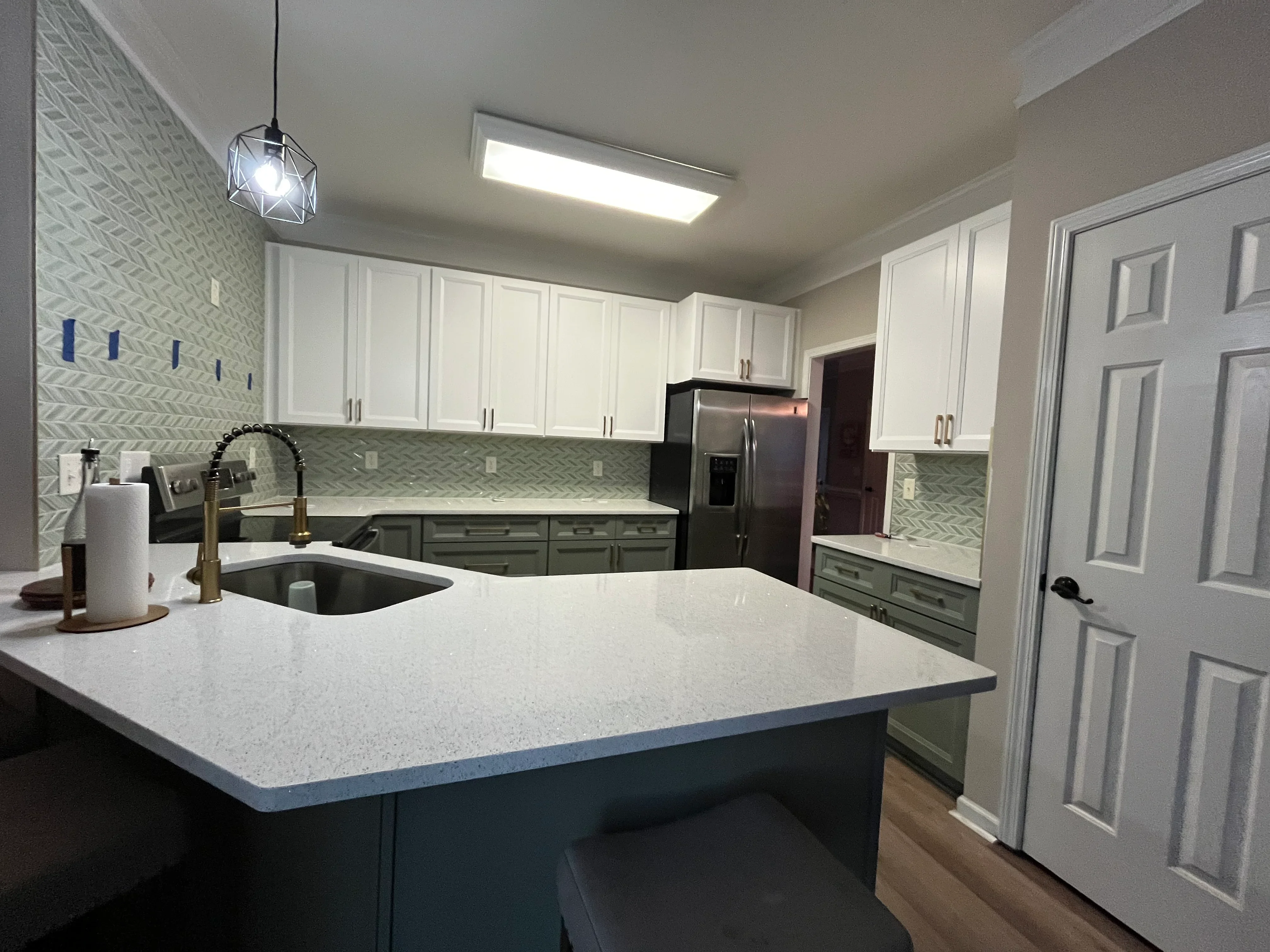 Modern kitchen with white and sage green cabinets, quartz counters, herringbone backsplash, and stainless steel appliances