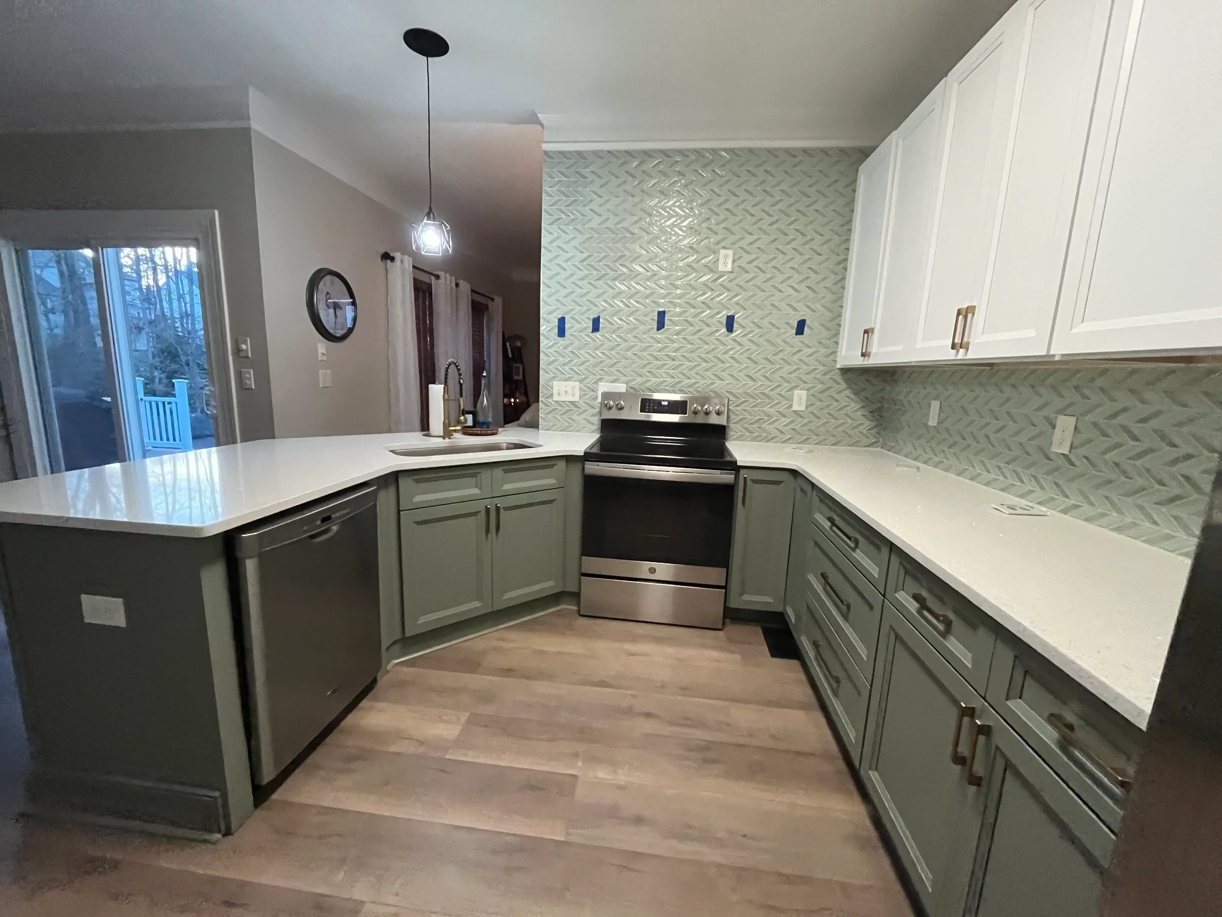 Kitchen with sage and white cabinetry, herringbone tile backsplash, quartz counters, stainless steel range